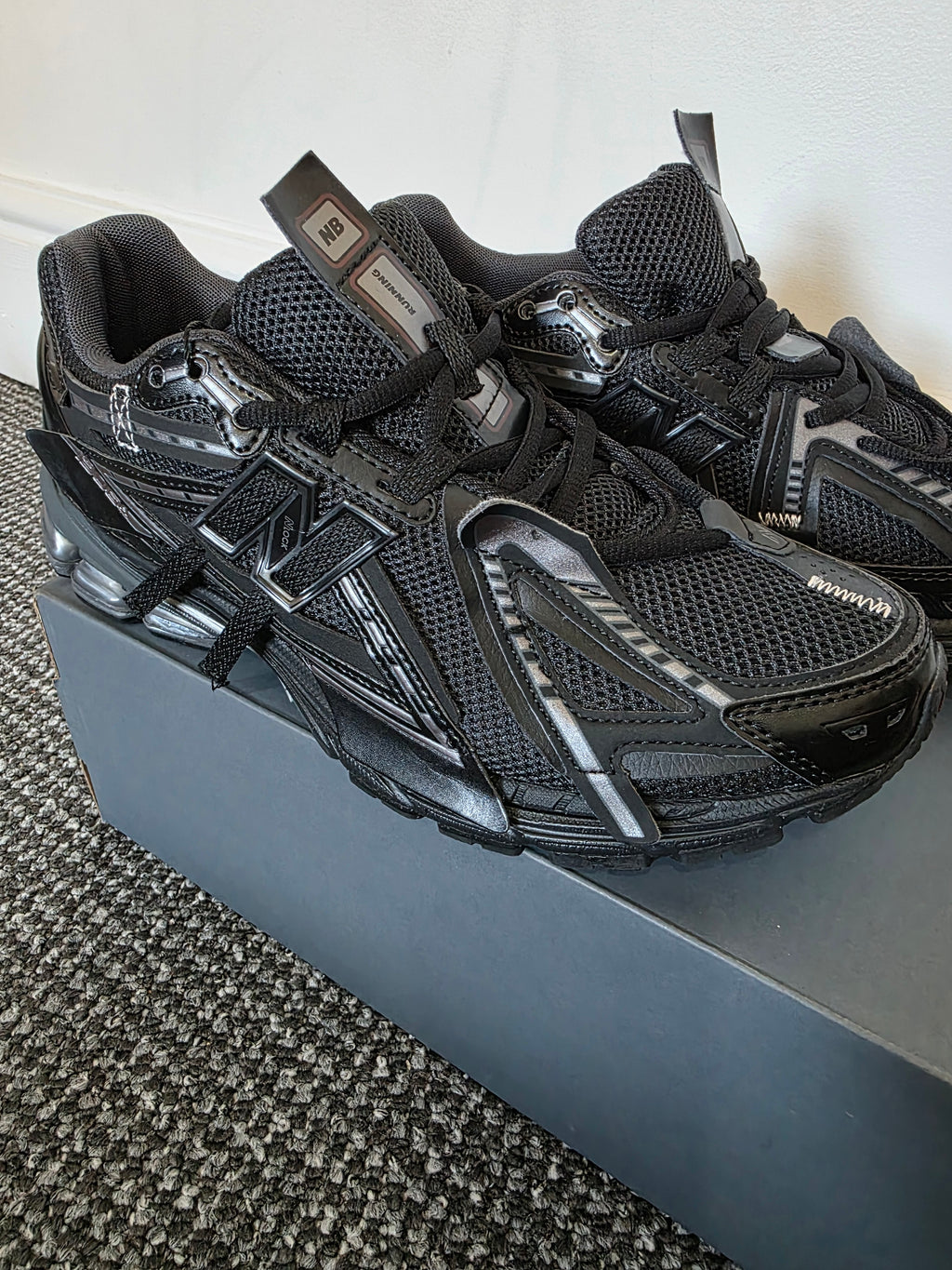 Stylish black sneakers featuring breathable mesh and synthetic overlays on a gray shoe box.